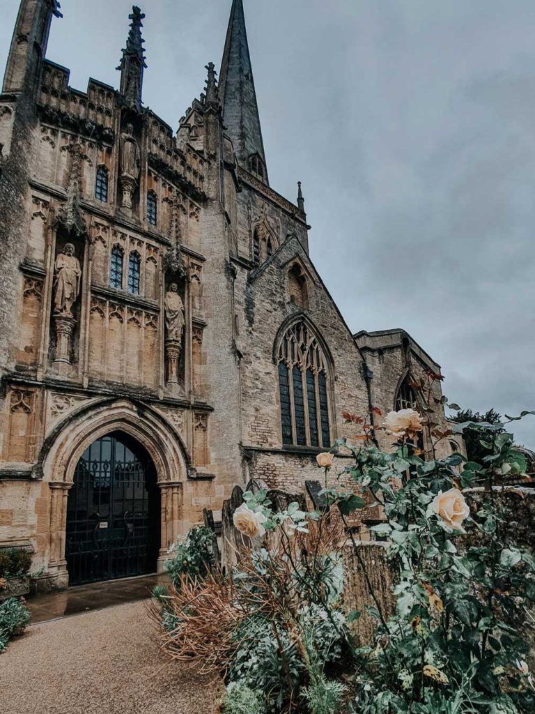 The exterior of St John the Baptist Church with rose bushes growing in the garden.