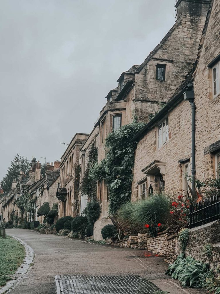 Homes along Burford Hill made out of Cotswolds stone. Some of the homes have flower bushes outside or ivy leaves growing on the exterior.