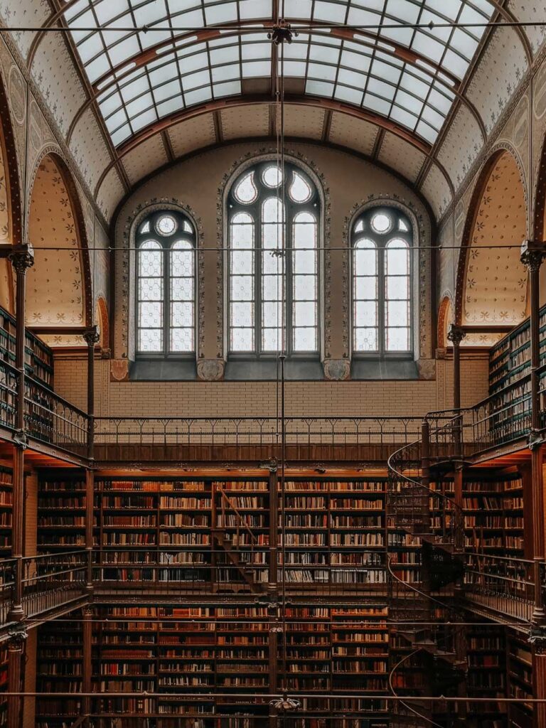 The Cuypers Library is a hidden spot inside the Rijksmusem in Amsterdam. 

From the balcony, you can see thousands of old books stored on the wooden shelves with a spiral staircase on the right side of the photo. 

The library has a glass ceiling alongside a large window at the top of the wall. To the sides, there are two more windows in a similar design (but smaller). 

There is also a black and white pattern on the ceiling. 