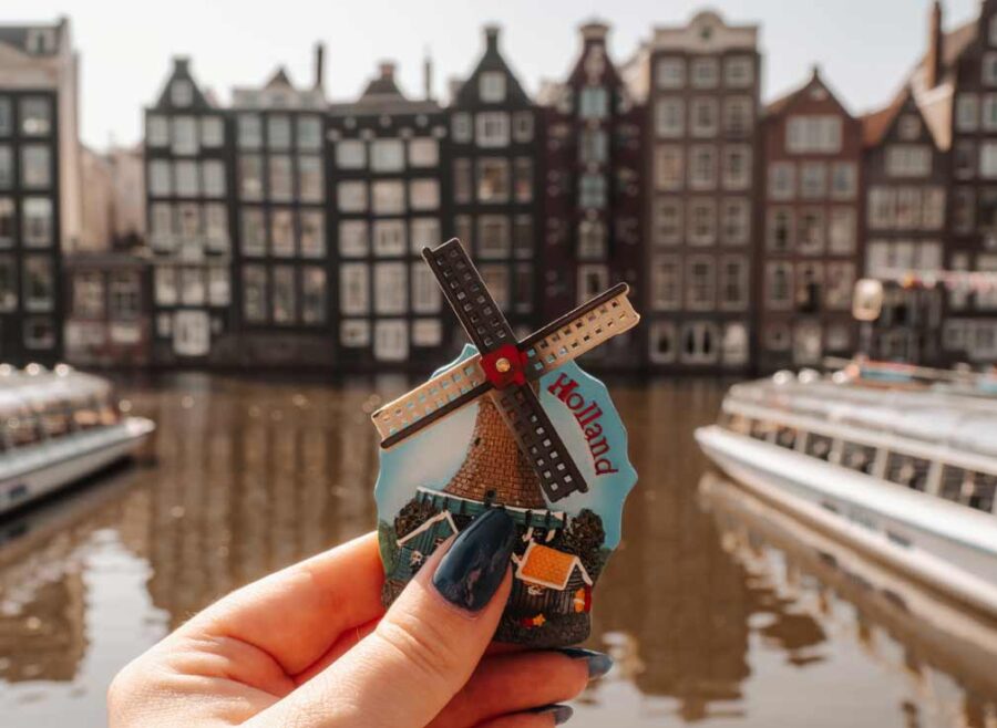 A woman holding a magnet in front of the canal and Damrak crooked houses. The magnet has a windmill on it and the windmill blades turn.