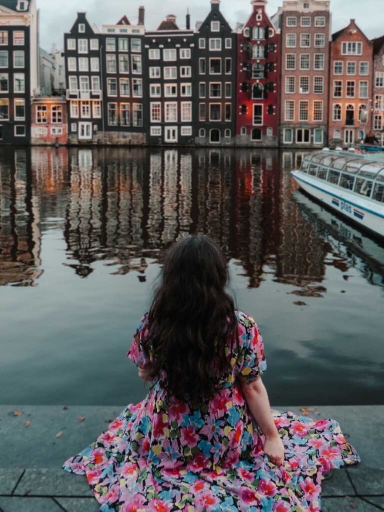 A brunette woman sat in front of the Damrak in Amsterdam