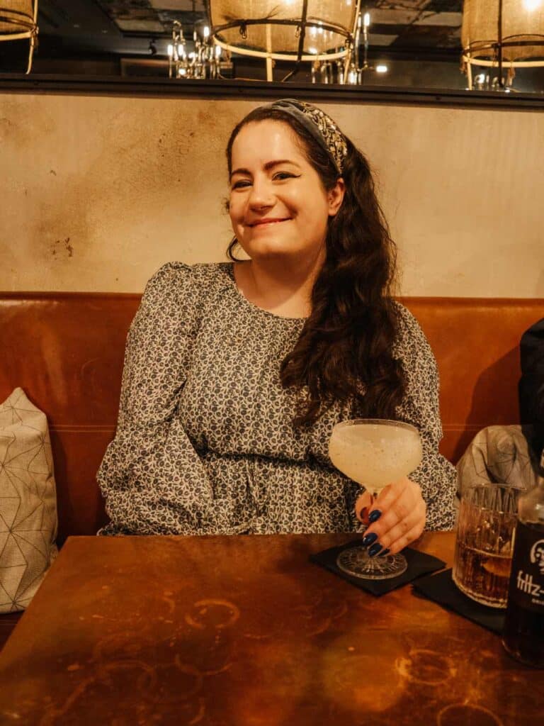 Lauren (the owner of this blog) enjoying a cocktail at Three Fingers Bar. Lauren is wearing a cream and blue floral dress and a blue sequined headband.