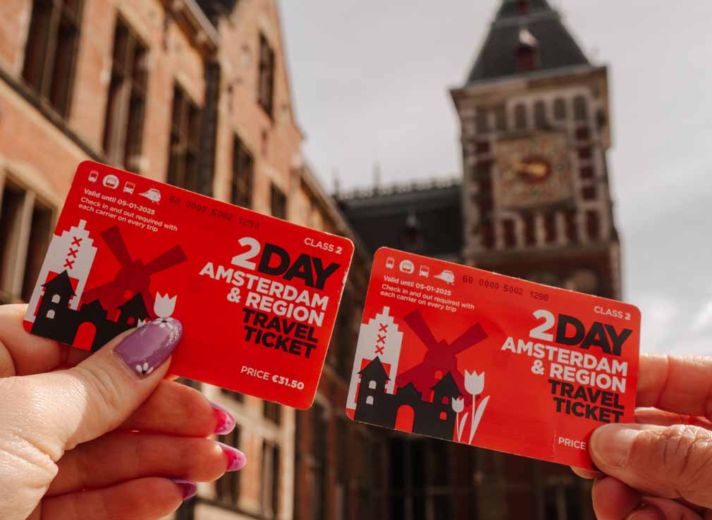 Two people holding their Amsterdam and Region Travel Tickets in front of Central Station