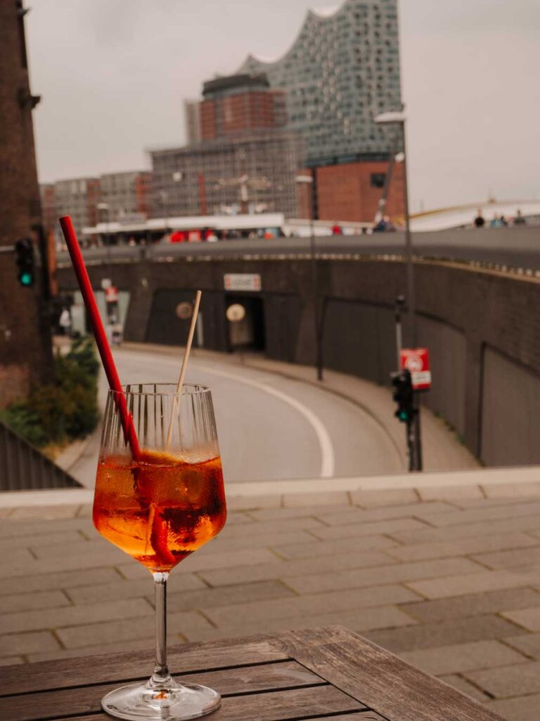 An Aperol Spritz sat on a table outside Alex Bar with views of Elbphilharmonie in the background.