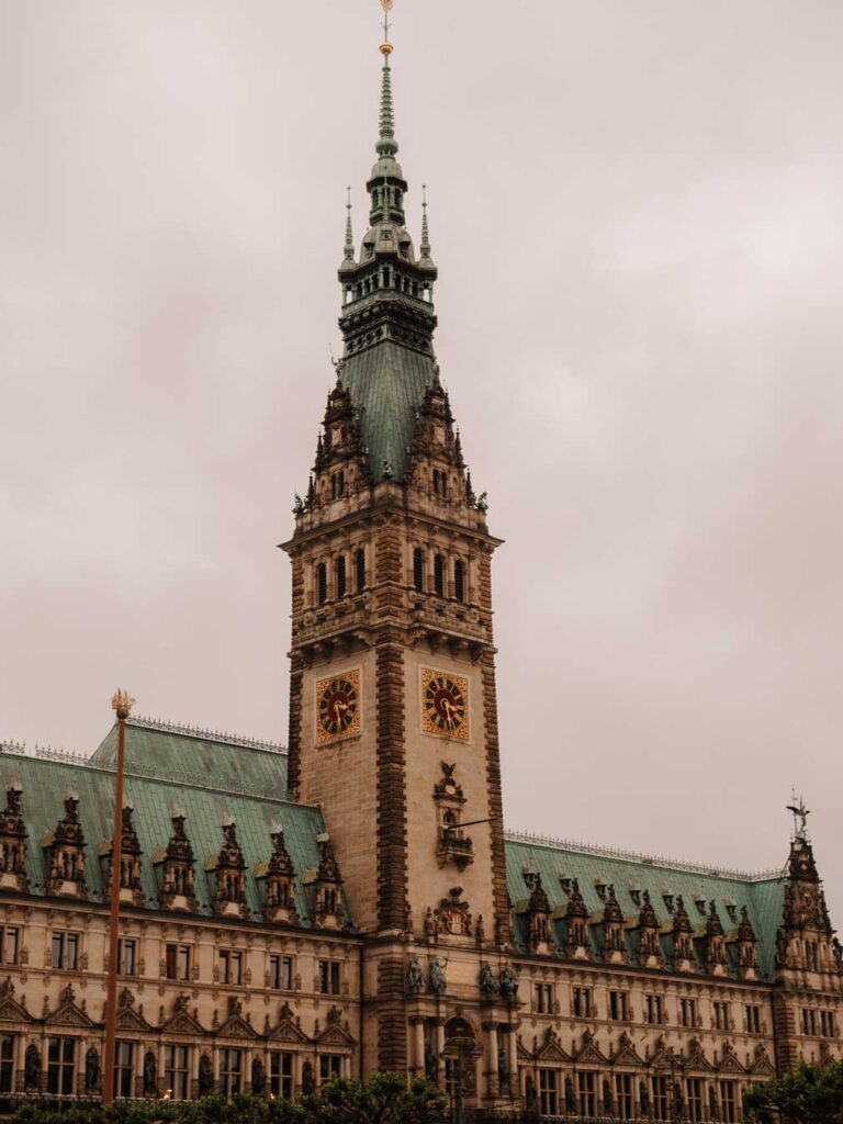 The City Hall in Hamburg features a prominent clock tower and spire rising above its green roof, showcasing a classic architectural design.