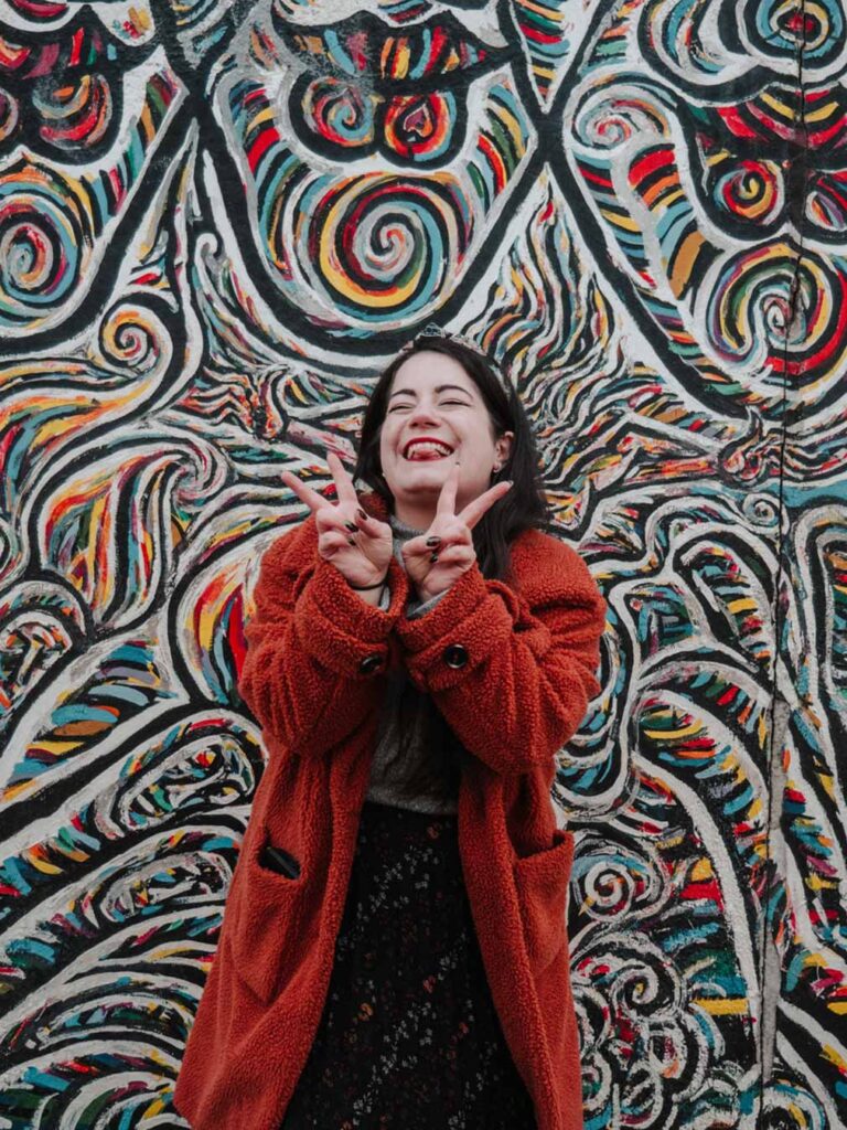 Lauren posing in front of a vibrant and colourful mural at the East Side Gallery in Berlin.
