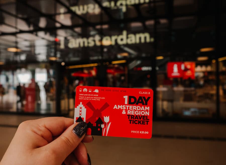 A person holding their Amterdam and Region Travel Ticket in front of the Iamsterdam store in Central Station