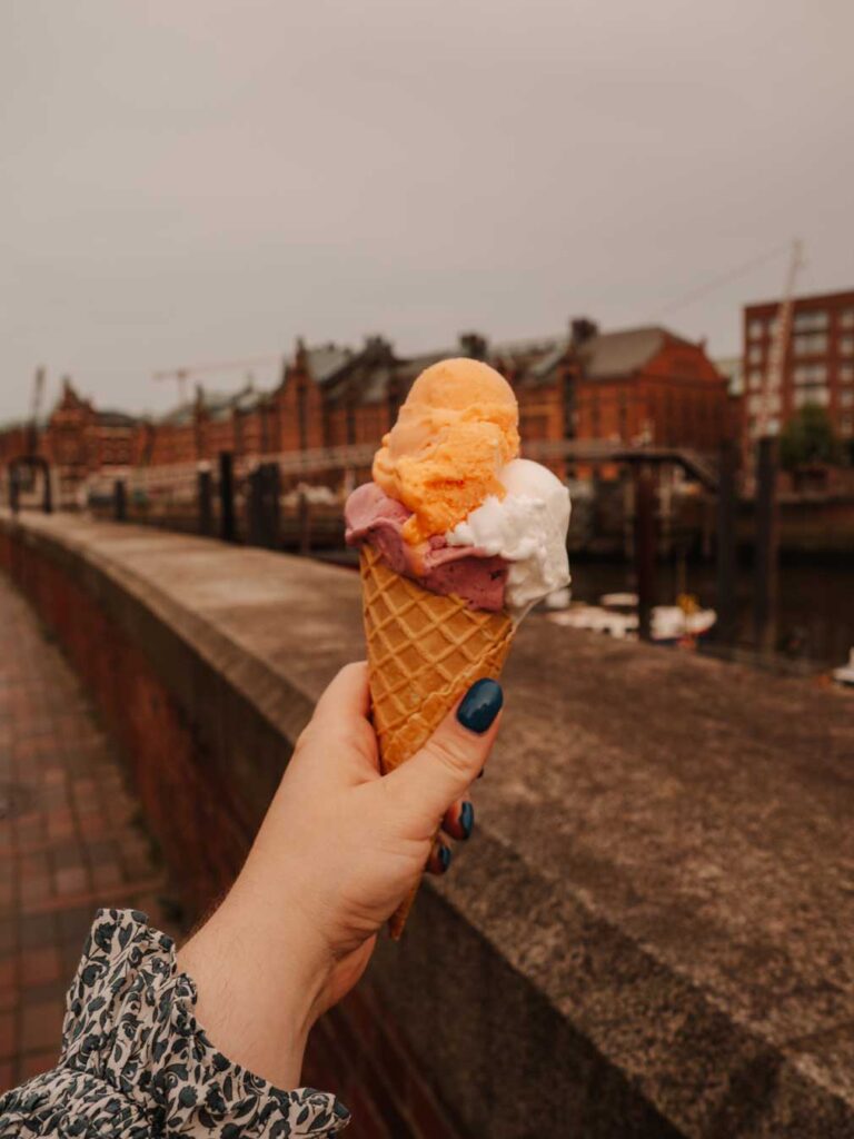 Lauren holding an ice cream cone in the Speicherstadt neighbourhood of Hamburg. In the distance, you can see the old brick warehouse buildings that Hamburg is known for.