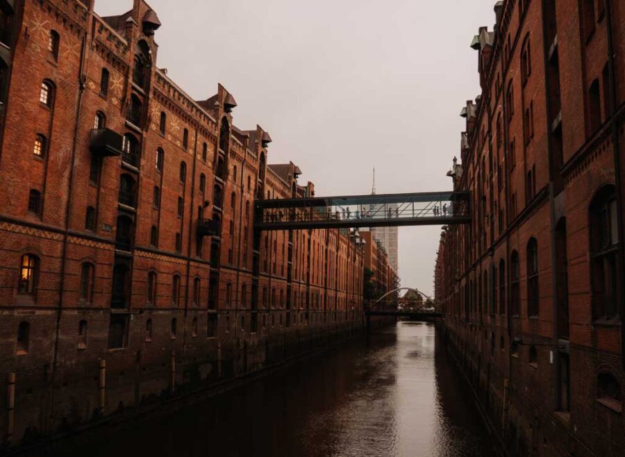 A serene canal flowing through Hamburg. It's surrounded by tall industiral brick buildings that reflect urban architecture and history in the Speicherstadt neighbourhood.