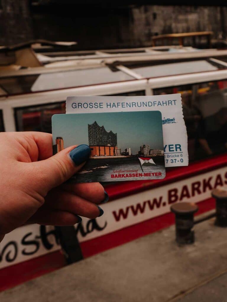 Lauren holding her tickets for the Port of Hamburg cruise. You can see the white and red boat in the background.