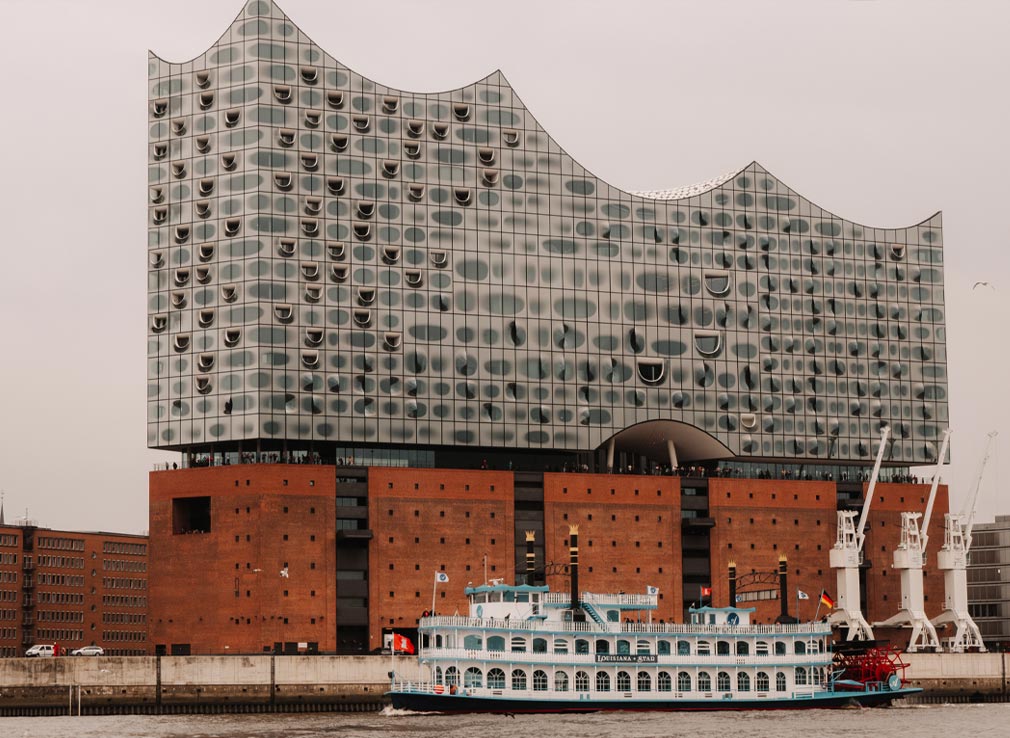 Views of Elbphilharmonie on a grey and overcast day. The Louisiana Star boat is also cruising along the port in front of the striking building.