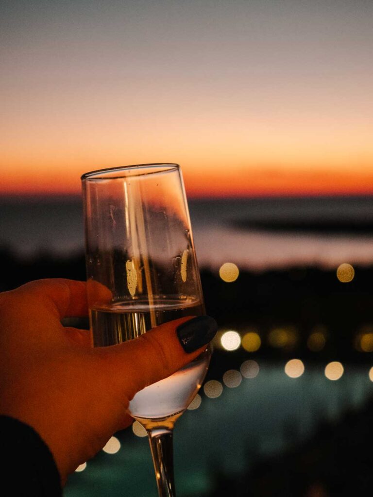 Lauren holding a glass of prosecco with sunset views from her balcony at Cali Resort and Spa.