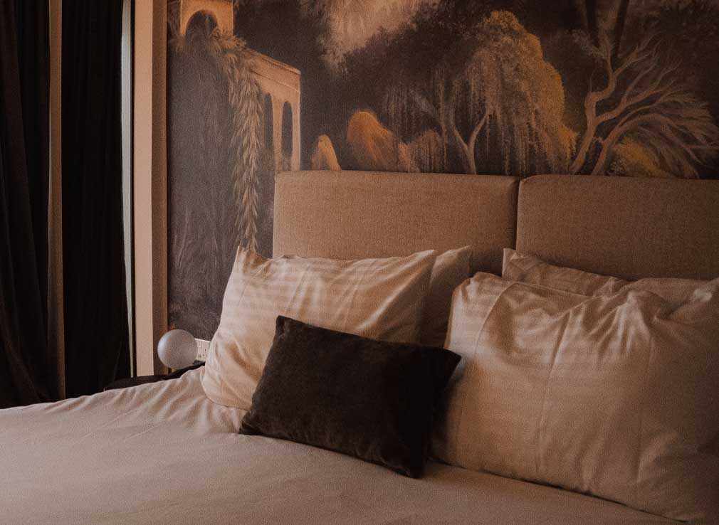 My bed at Cali Resort and Spa with white bedding, a green velvet cushion and an impressive wallpaper mural in the background.