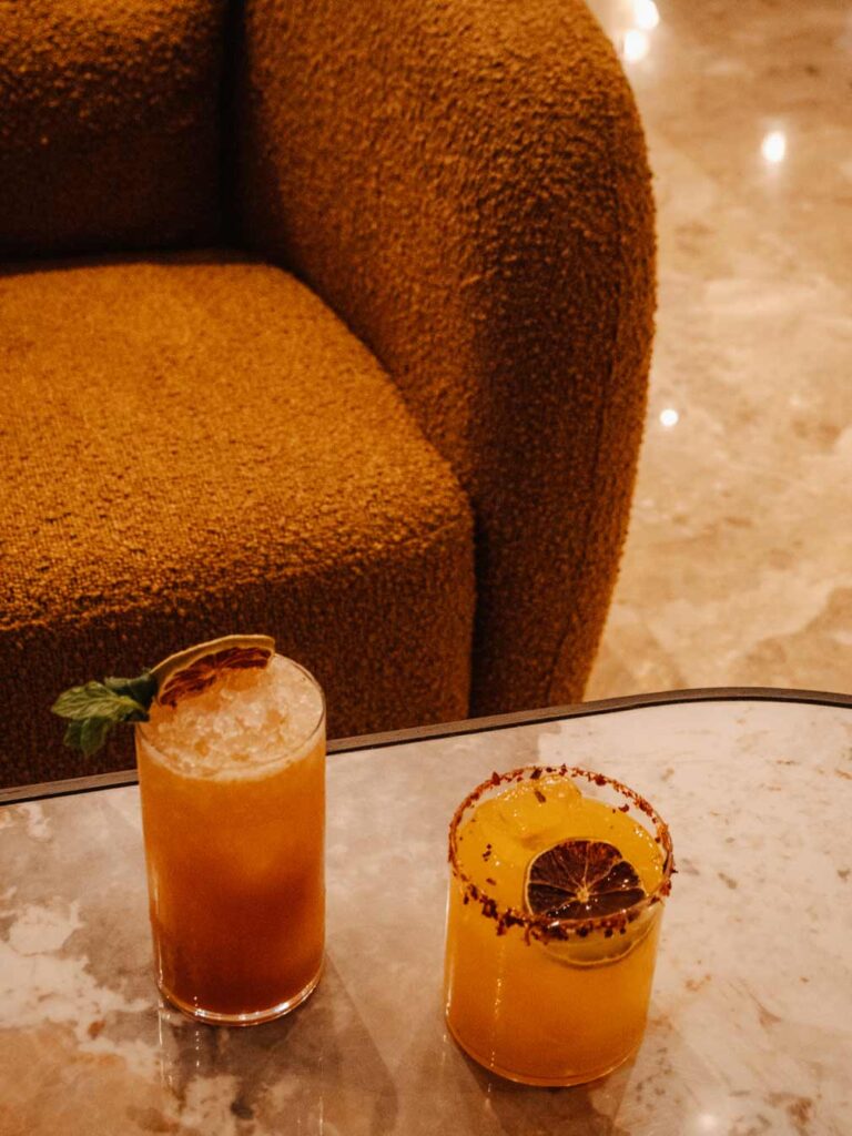 Cocktails from Sonata Lounge sitting on a marble table with a rust orange boucle chair in the background.