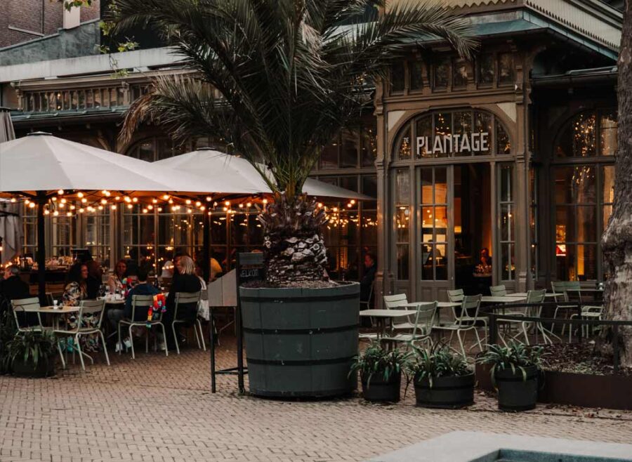 The exterior of De Plantage in Amsterdam with some people dining on the patio.